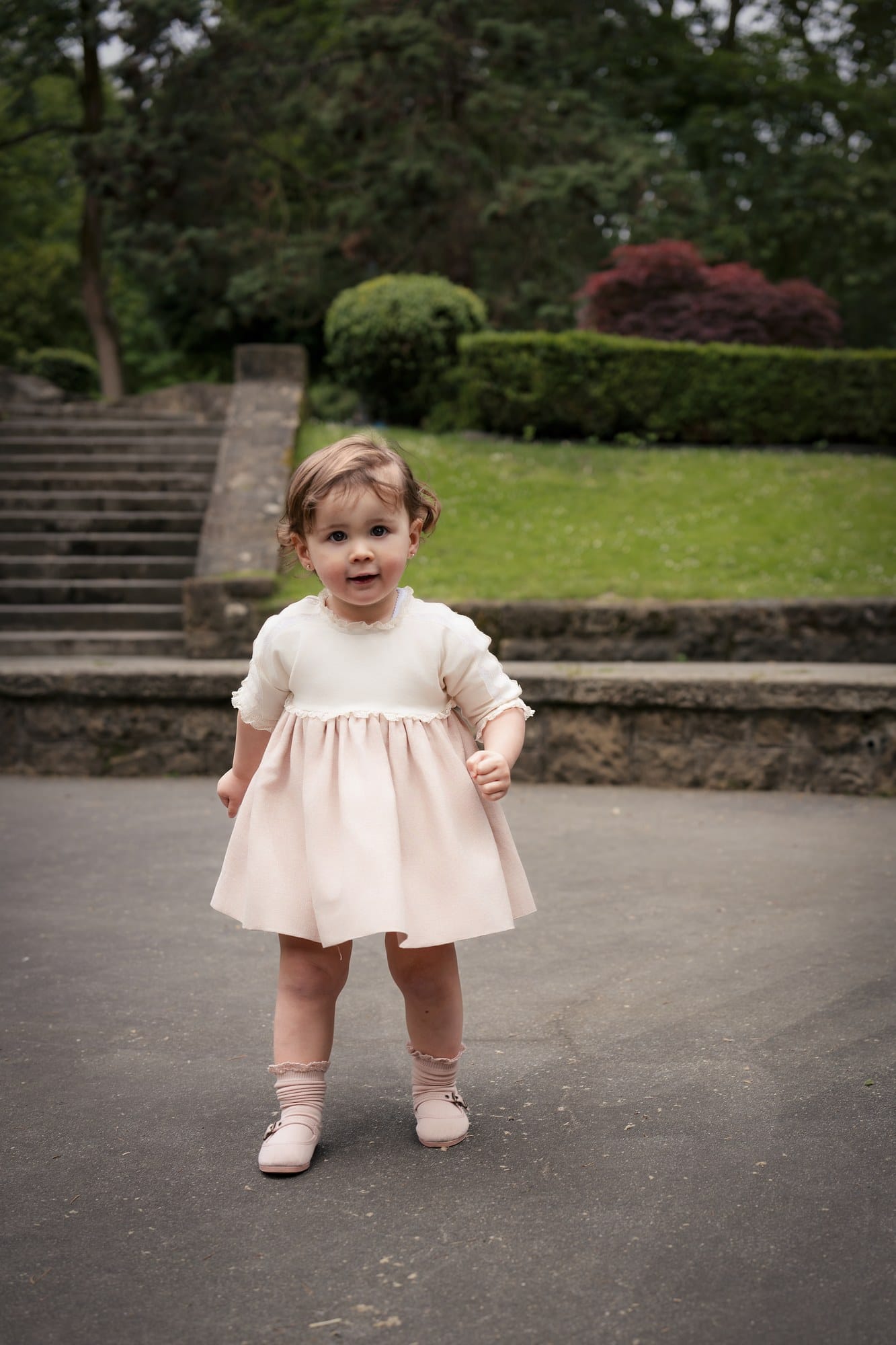 Niña pequeña de pie en un parque, con vestido rosa