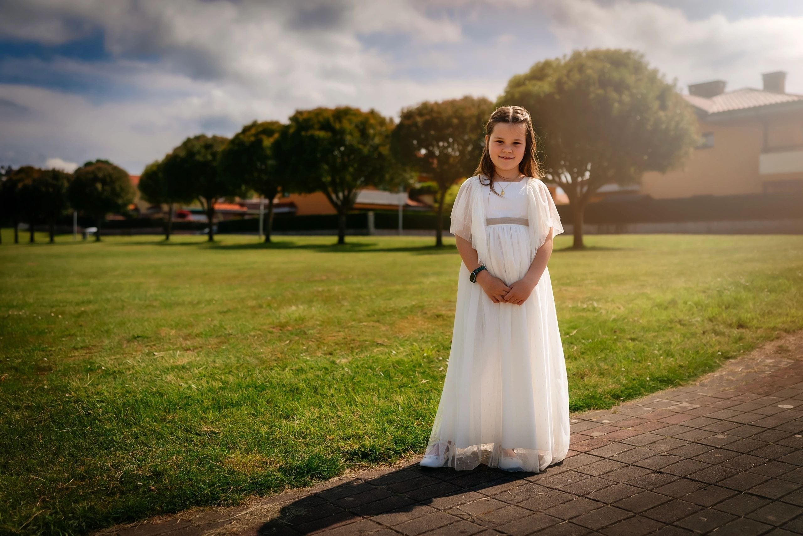 Niña de comunión de pie sola en un prado, al atardecer