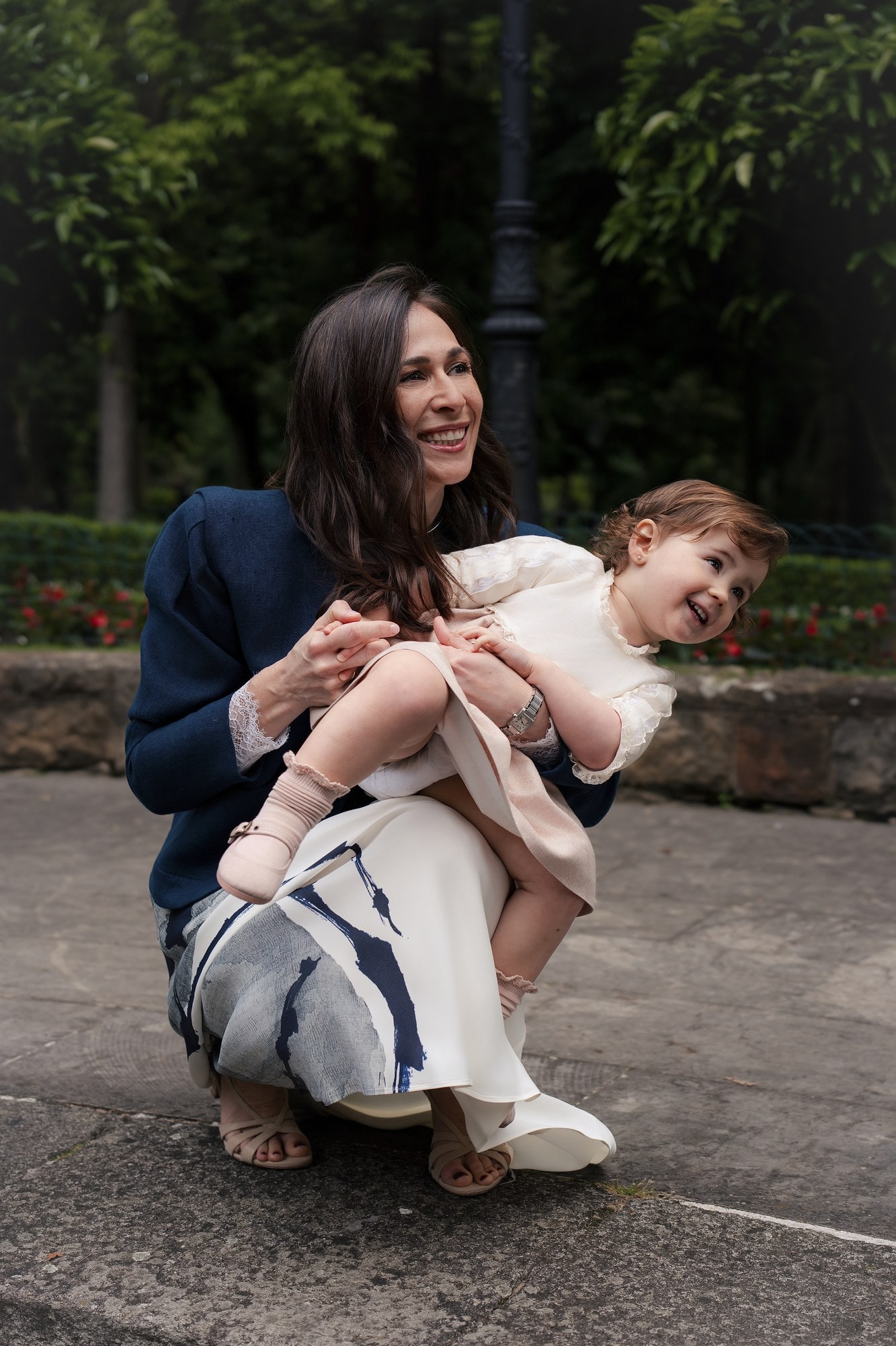 Una madre levanta en brazos a su hija pequeña, riendo, en un parque