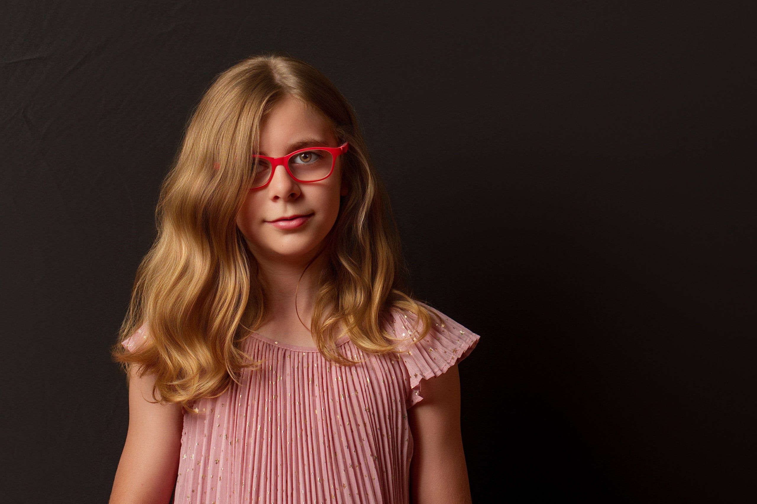 Retrato de una niña con gafas rojas, sobre fondo oscuro