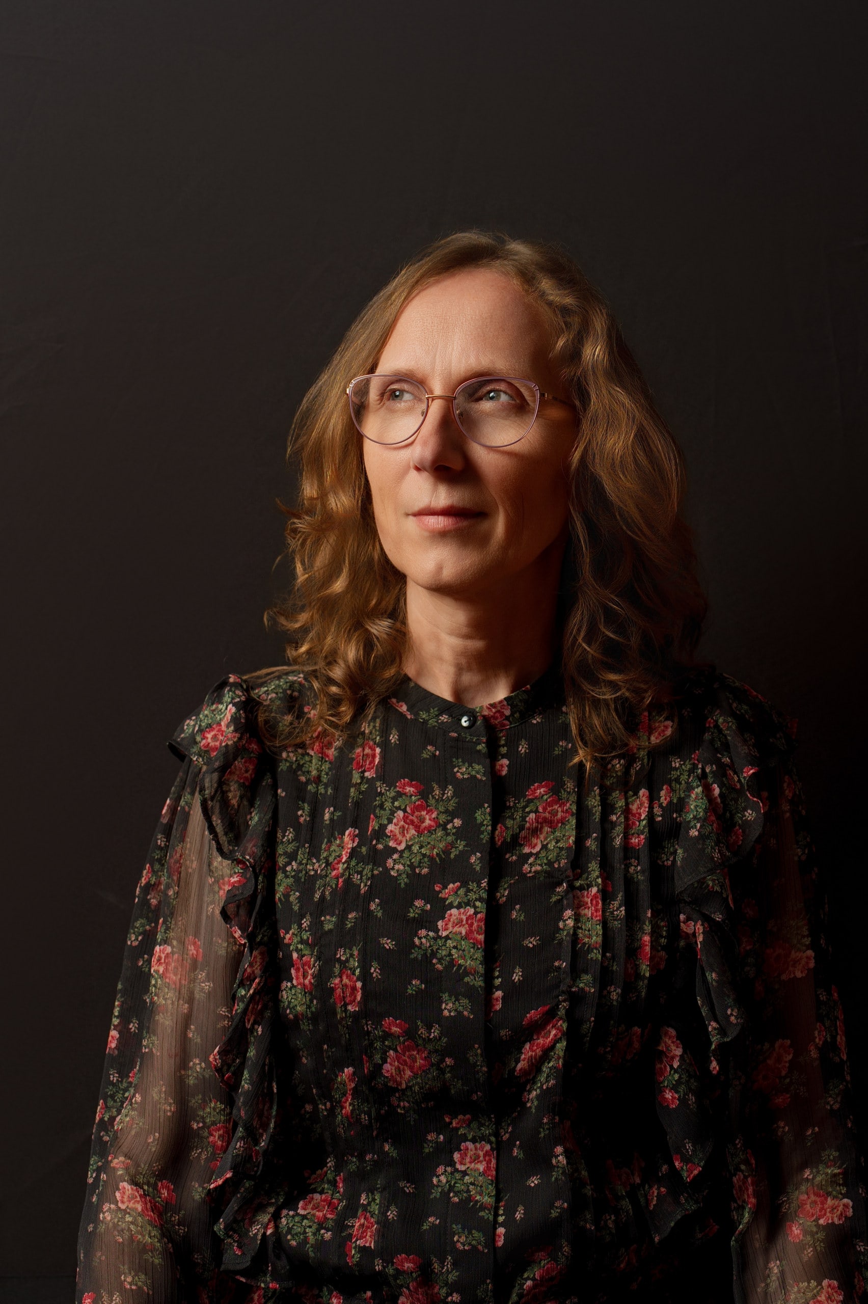 Retrato de una mujer con gafas y vestido de flores, sobre fondo oscuro